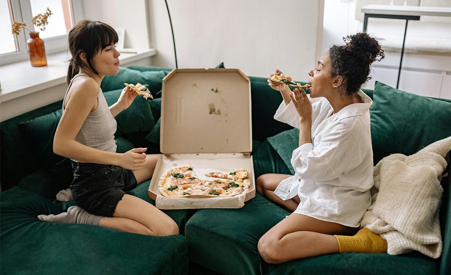 dos mujeres sentadas en el sofa comiendo una pizza